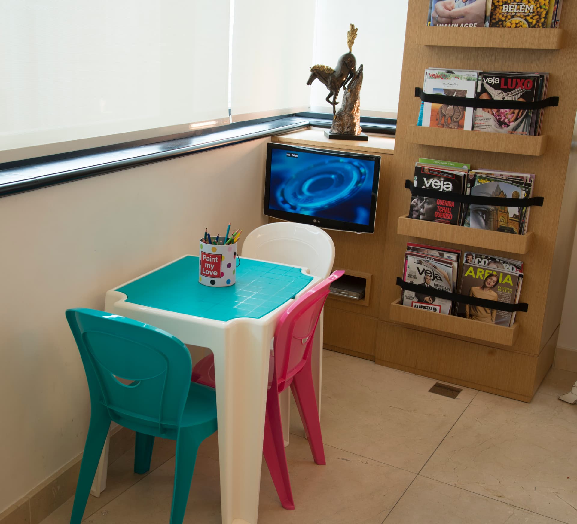 Espaço infantil da sala de espera com mesa de desenho e revistaria